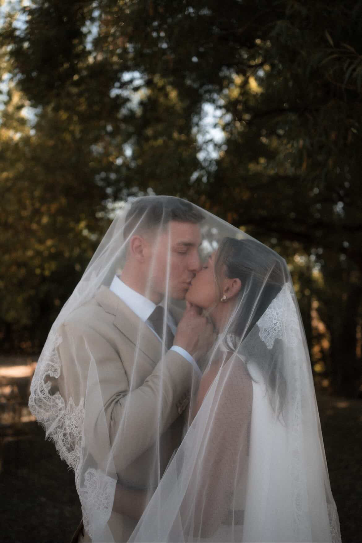 Bride and groom kissing beneath a lace veil